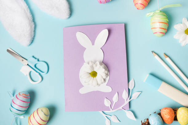 istock Diy Easter card from paper. greeting cards with bunny on blue background. Gift idea, decor Spring, Easter. Top view. Process kid children craft. 1303841431