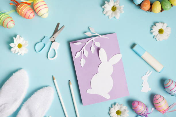 istock Diy Easter card from paper. greeting cards with bunny on blue background. Gift idea, decor Spring, Easter. Top view. Process kid children craft. 1303841436