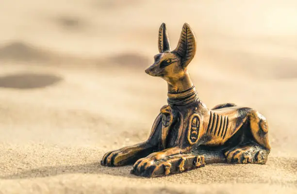 Traditional souvenir. An intaglio ceramic figurine of the ancient Egyptian god of death Anubis, half-sherk-half lion against the backdrop of the hot sands of the Sahara Desert in North Africa. Tourist trip to the sights of Egypt