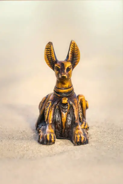 Traditional souvenir. An intaglio ceramic figurine of the ancient Egyptian god of death Anubis, half-sherk-half lion against the backdrop of the hot sands of the Sahara Desert in North Africa. Tourist trip to the sights of Egypt