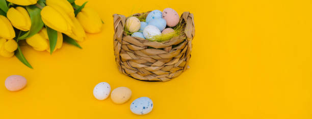 istock Easter holiday web banner on yellow background. Colorful easter painted speckled eggs in basket. Creative spring composition with Easter elements - flowers and eggs. Traditional Easter Celebrating 1303842161