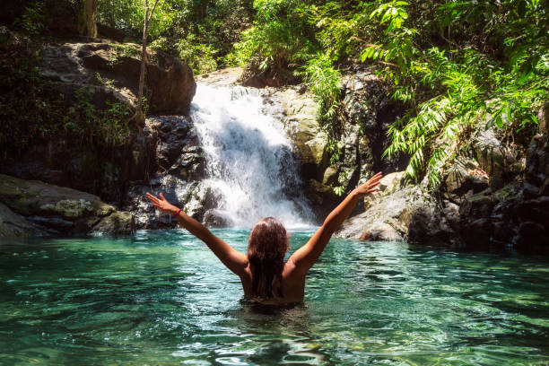 bella ragazza a braccia aperte vicino a una cascata in una foresta tropicale. - number of people human gender people waterfall foto e immagini stock