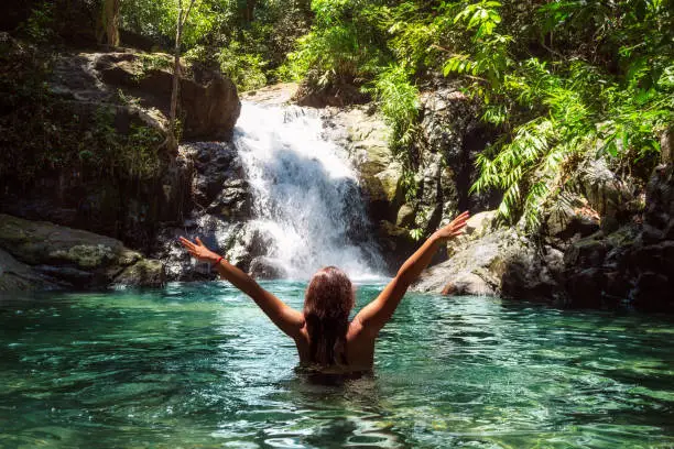 Beautiful girl in a swimsuit with open arms near a waterfall in a tropical forest.