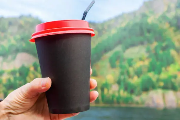 Photo of Woman holding a black cup with coffee on the background of a beautiful landscape
