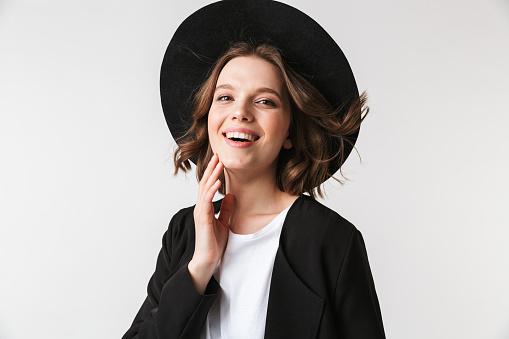 Portrait of a laughing young woman dressed in black jacket and sunglasses posing while standing isolated over white background