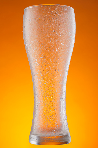 Empty Drinking glass. Ice Cold Beer Glass With Water Drops Condensation on orange Background