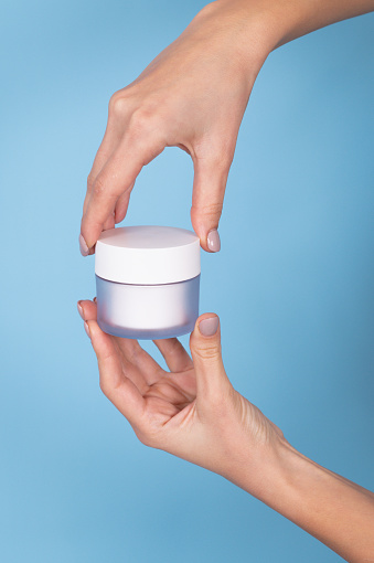 Female hands with perfect manicure holding cream bottle of lotion or face cream. Empty jar cosmetic products on blue background. Skin care concept. High quality photo