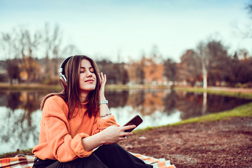 Beautiful Female Closing Eyes While Enjoying Favorite Song In Park On Headset
