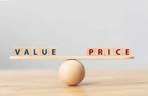 Wooden seesaw scale empty on wooden sphere on wood table with wording VALUE and PRICE balancing