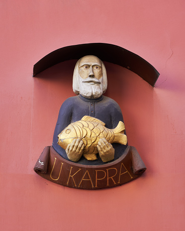 Prague, Czech Republic - March 2, 2020 Rustic wood carving depicting old man holding a carp fish on a wall in Karlova Street