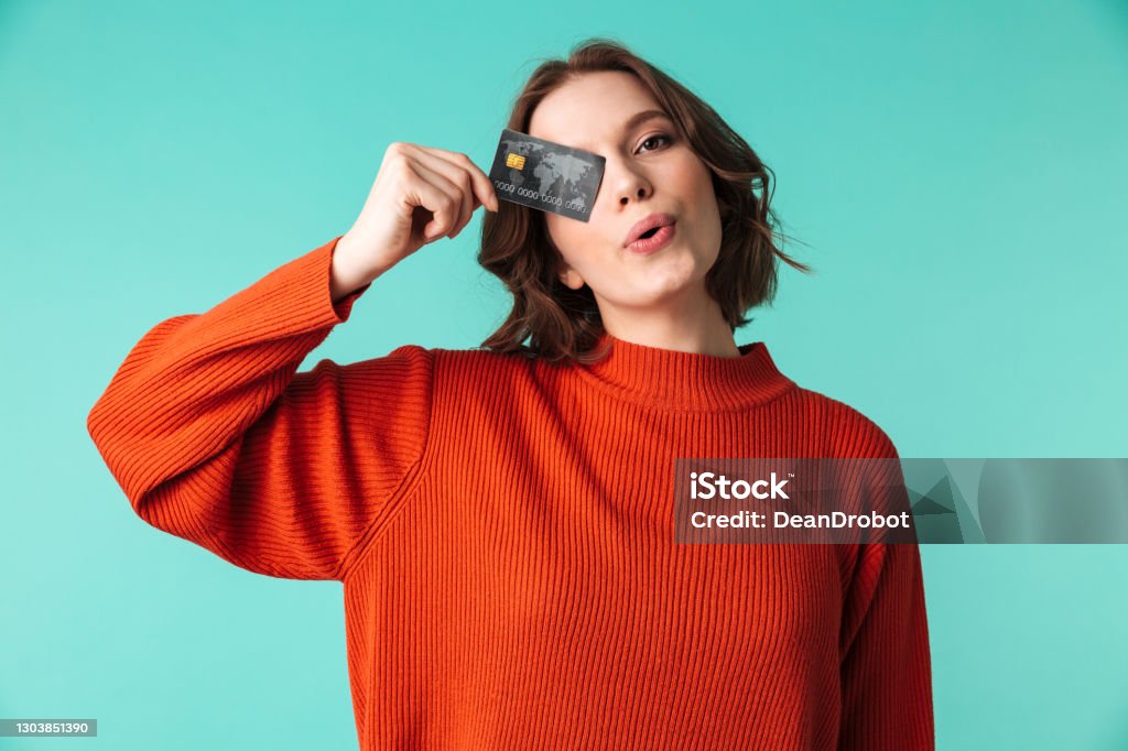 Portrait of a pretty young woman dressed in sweater Portrait of a pretty young woman dressed in sweater holding credit card at her face isolated over blue background Credit Card Stock Photo