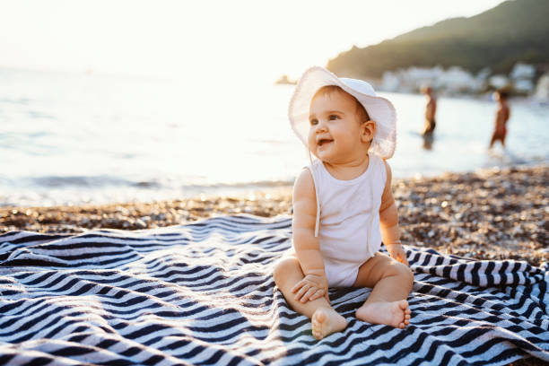 Baby girl with hat sitting on towel at the beach in summer stock photo