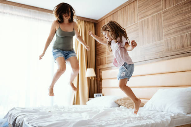 istock Millennial mother and daughter jumping on bed while holding hands 1303852539