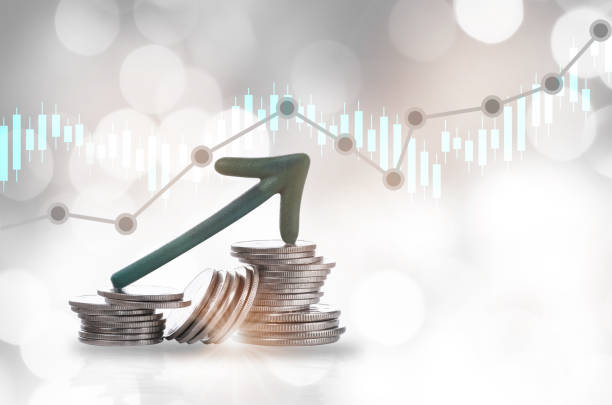 Green arrow upward on stack of coins and growth graph on bokeh background stock photo