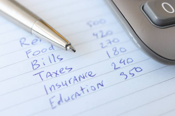 istock Monthly expenses are listed in notebook next to pen and calculator 1303855111