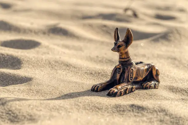 Photo of Ceramic statuette of the Egyptian god Anubis against the backdrop of sunny sands