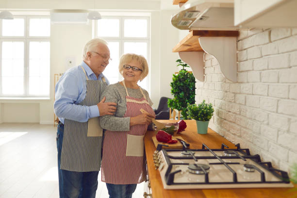 couples aînés heureux cuisinant le repas végétarien sain restant au comptoir dans la cuisine - stove top photos et images de collection