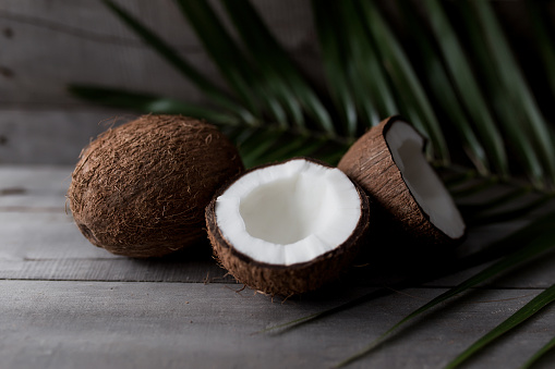 Broken coconuts on gray wooden background with palm leaf. White coconut pulp. High quality photo
