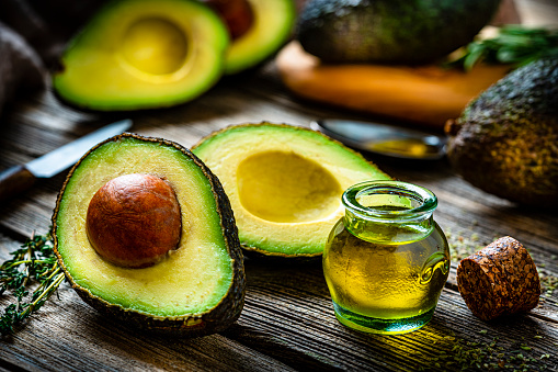 Vegan food: extra virgin avocado oil in a glass container shot on rustic wooden table. Sliced and whole organic avocados complete the composition. Predominant colors are yellow and green. High resolution 42Mp studio digital capture taken with Sony A7rII and Sony FE 90mm f2.8 macro G OSS lens