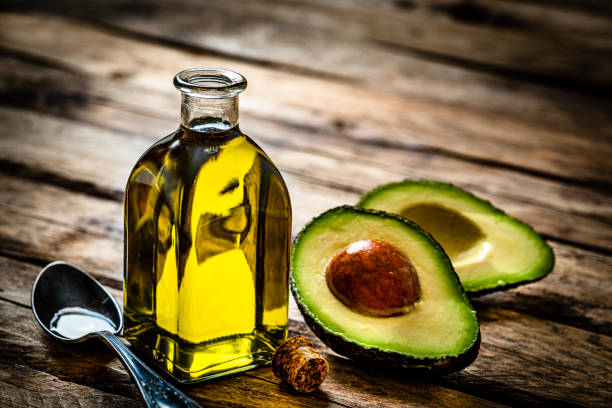 Avocado oil on rustic wooden table Vegan food: extra virgin avocado oil in a glass bottle shot on rustic wooden table. Sliced organic avocado and a spoon filled with oil are beside the bottle. Predominant colors are yellow and green. High resolution 42Mp studio digital capture taken with Sony A7rII and Sony FE 90mm f2.8 macro G OSS lens avocado brown stock pictures, royalty-free photos & images