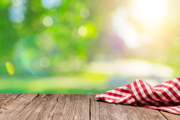 istock Empty rustic picnic table with crumpled gingham cloth against defocused nature background 1303865779