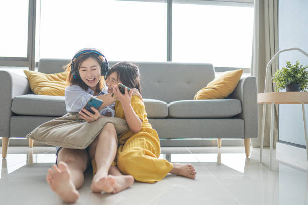 Asian Chinese mother and daughter enjoying bonding time in living room listening to music with phone headphone stock photo