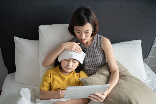 Asian Chinese mother using digital tablet communicate with doctor pediatrician on her daughter sickness