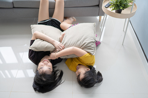 2 Asian Chinese sibling sister bonding playing on floor in living room with pillow cushion during weekend