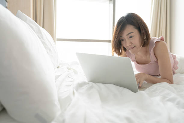istock Asian Chinese mature woman lying on bed using laptop. Relax 1303867713