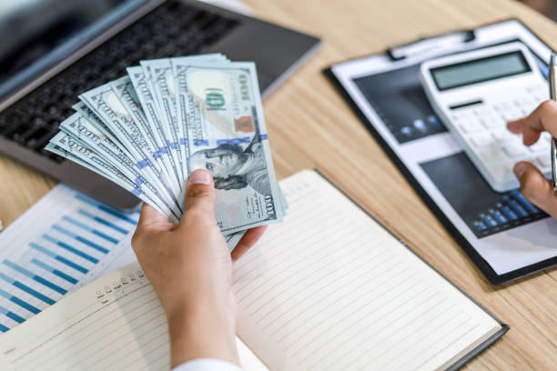 istock A man is pressing a white calculator with his right hand and holding a dollar with his left hand. 1303870695