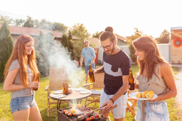 Friends grilling meat at backyard barbecue party Group of cheerful young friends having fun at backyard barbecue party, grilling meat, drinking beer, playing badminton and relaxing on a sunny summer day outdoors barbecue stock pictures, royalty-free photos & images