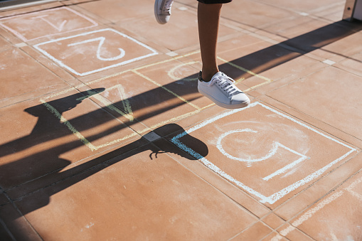 Cute and gorgeous child playing in the school yard jumping on a hopscotch.