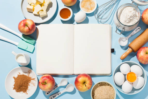istock Cooking baking background with empty cookbook, ingredients, fresh apples, spices and utensils on blue table. 1303878842