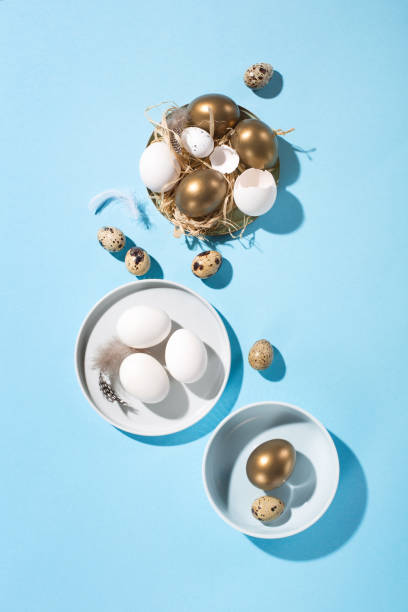 istock Easter white golden eggs, quail eggs and feathers on blue background. 1303878885
