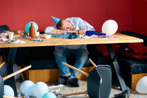 istock Man sleeping at table with blue cap in messy room after birthday party 1303880034