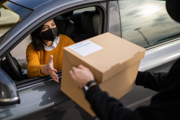 Woman with face mask picking order from her car at a Curbside pickup Young woman wearing face mask and picking order from delivery guy while sitting in car at a Curbside pickup curbsidepickup stock pictures, royalty-free photos & images