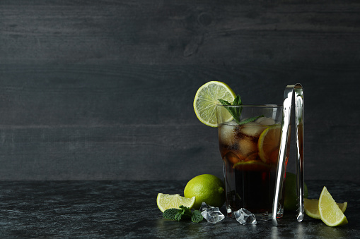 Glass of Cuba Libre and ingredients on dark background