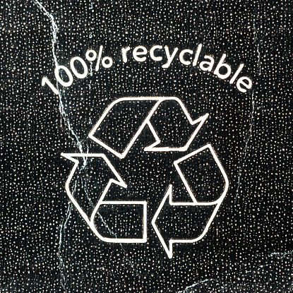 A macro image of a recycling triangle symbol on patterned cardboard.