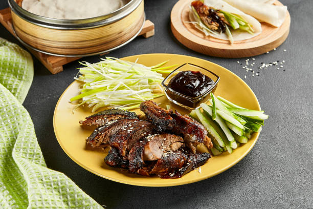 Peking duck chinese food. Yellow plate with vegetables and sauce on dark slate table. Chinese, asian, authentic food concept Peking duck chinese food. Yellow plate with vegetables and sauce on dark slate table. Chinese, asian, authentic food concept. hoisin sauce stock pictures, royalty-free photos & images