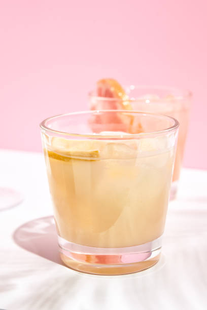 istock White alcohol cocktail over pink wall background. DRink with lemon on white table in sunshine with hard shadow of palm leaf. Alcohol, summer, fresh cocktail concept 1303888770