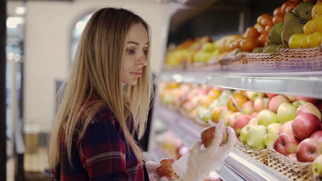 Woman in glove picks fruits apples in basket in supermarket