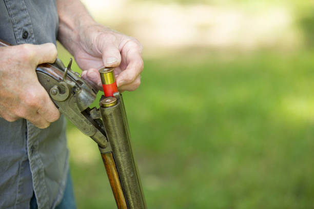 Senior Man  loading an antique 12 gauge double barred shot gun.  He is testing it prior to purchase or sell.  He is outside, green grass in background.