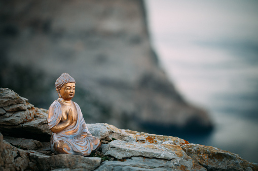 Buddha figure sitting on a rock in front of mountains and the mediterranean sea on Majorca. Part of a series.