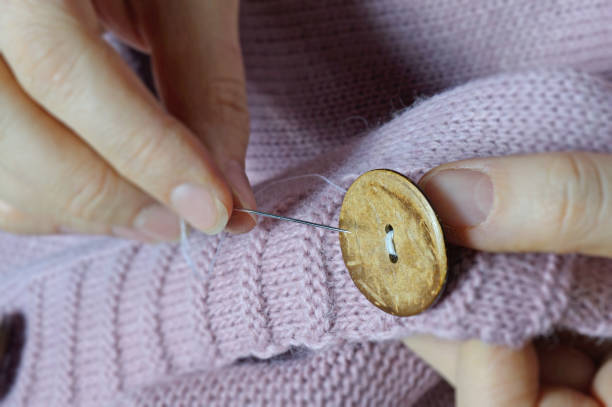 istock female workers' hands sew a wooden button to a jacket. close-up. 1303897974