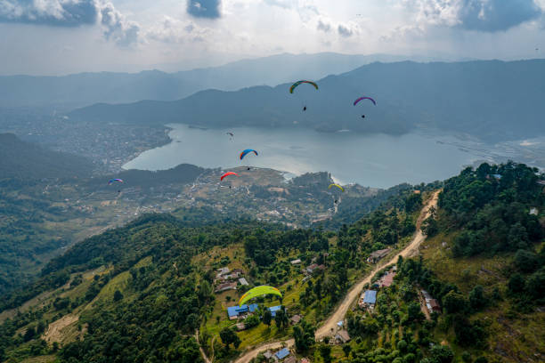 Paragliders sail over mountains and lake on a stormy day Lush forest and town below airborne sport stock pictures, royalty-free photos & images