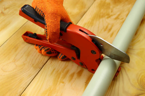 istock Gloved hand cuts pvc water pipe with scissors on wooden background 1303899380