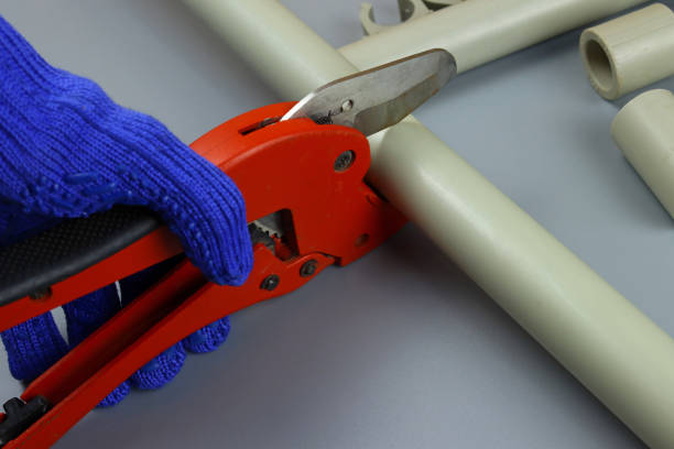 istock Gloved hand cuts pvc water pipe with scissors on gray background 1303900215