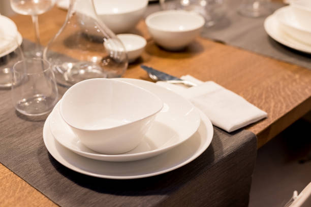 istock Table with plates and glasses before a party.Piles of white ceramic tableware, plates, saucers, cups on a wooden table. kitchenware.Festive table 1303900662
