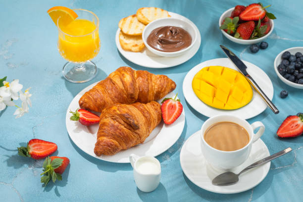 istock Luxury sunny continental breakfast on blue concrete background table with tropical plants shadows 1303901888
