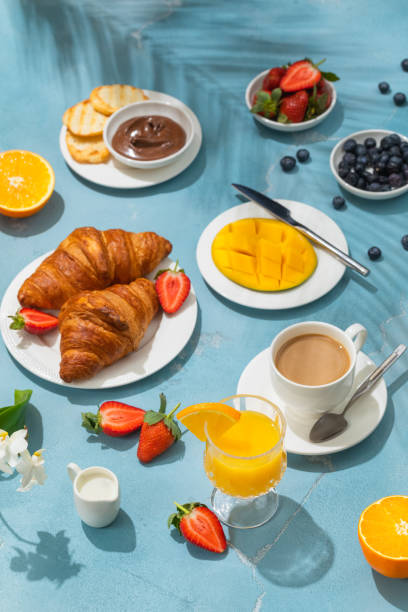 istock Luxury sunny continental breakfast on blue concrete background table with tropical plants shadows 1303901891